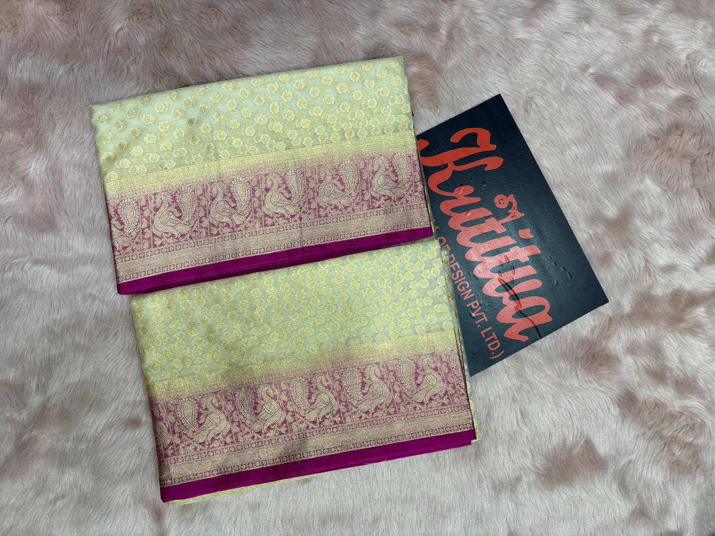 Traditional saree with a purple border on a textured surface, featuring a visible brand name.