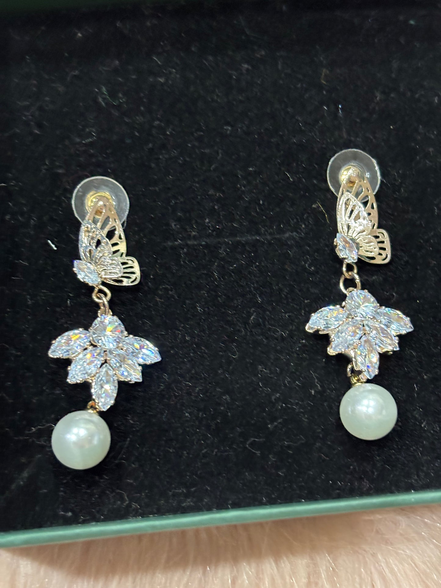 Pair of earrings with floral designs and pearls on a black background