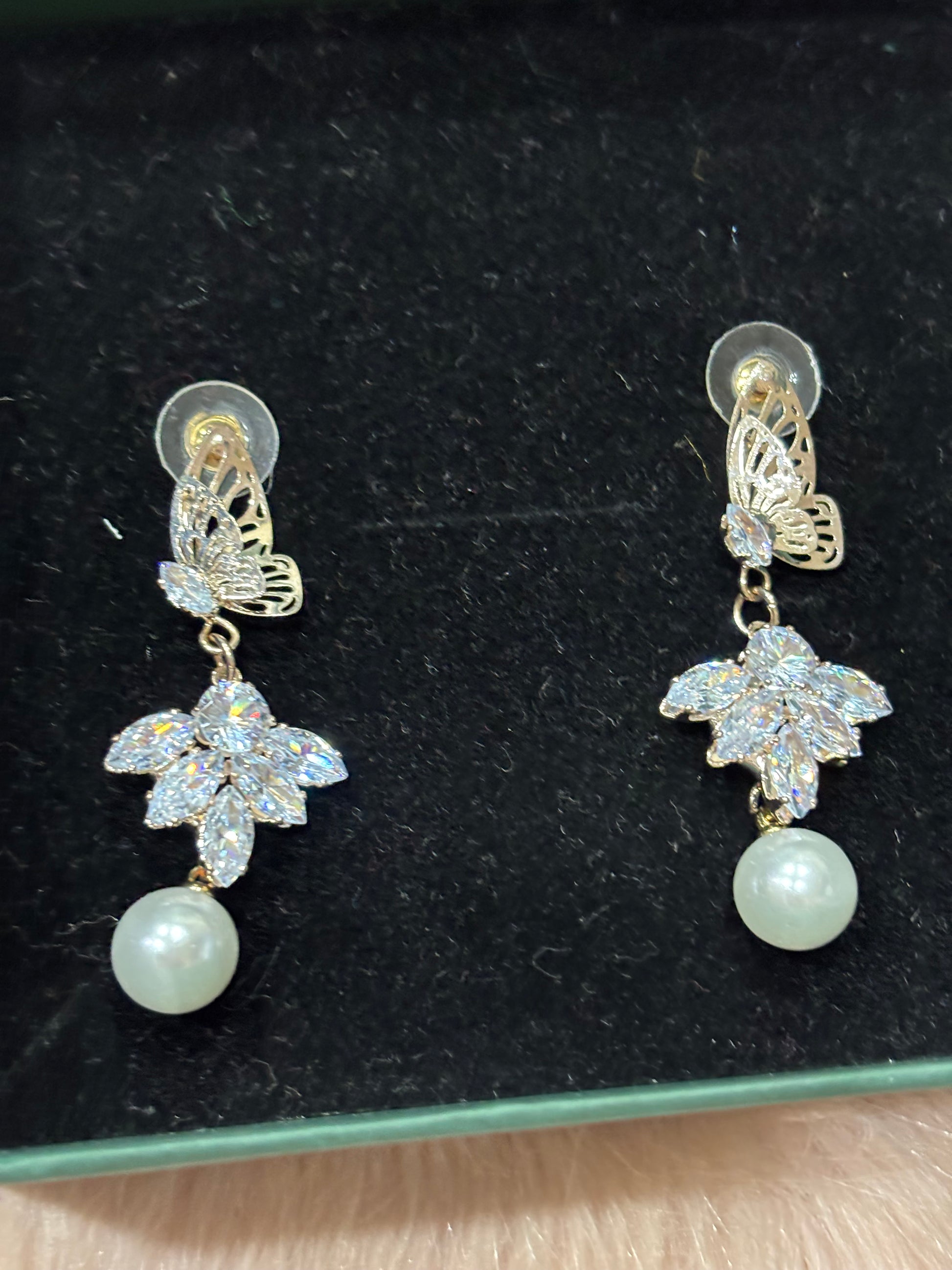 Pair of earrings with floral designs and pearls on a black background