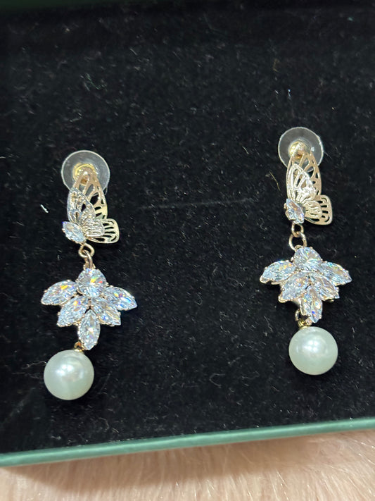 Pair of earrings with floral designs and pearls on a black background
